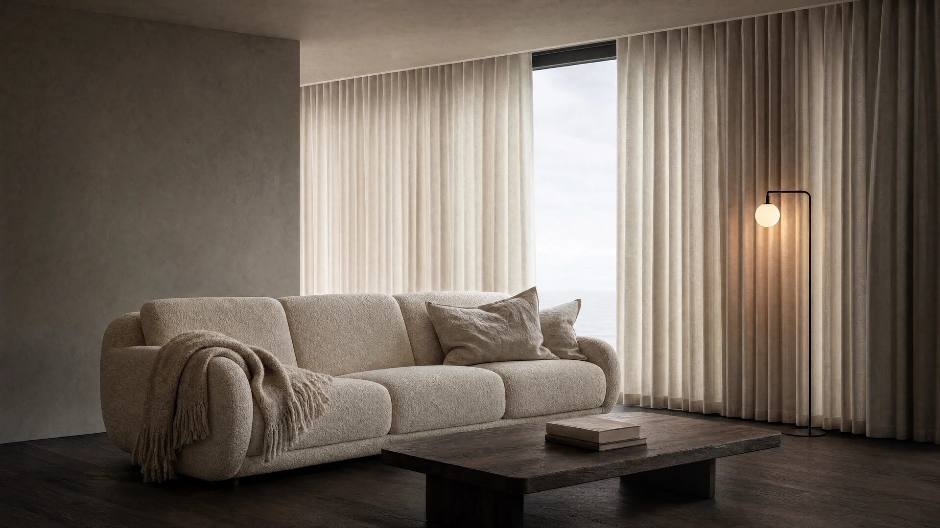 A living room with a cream bouclé sofa and sheer linen curtains beside a sea-view window