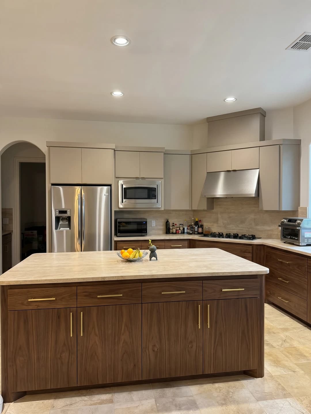 The same kitchen resurfaced with walnut and greige two-tone cabinets, a matching walnut island, and honed travertine surfaces, an iova visual